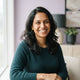 A professional portrait of a smiling South Asian mother, representing a happy customer in a modern, light-filled setting.
