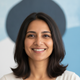 Smiling South Asian woman's authentic portrait headshot, against a soft, subtly blurred backdrop in slate blue and bright whi